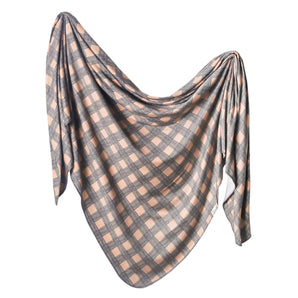 The Copper Pearl Billy is a cozy knit swaddle blanket with a gray and peach checkered pattern on a crisp white background.