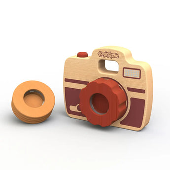 The Shutterbug Camera by Begin Again is crafted from sustainably sourced rubberwood and boasts a charming design with a red lens knob and three interchangeable side discs. Its two-toned wood features light and dark brown accents, with the brand name elegantly displayed on top.