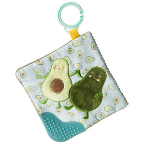 The Mary Meyer Crinkle Teether, Avocado, is a soft square toy featuring two smiling avocado characters on a light green background with small patterns. It includes a blue crinkle teether corner and a mint green attachment ring, ensuring baby safety.