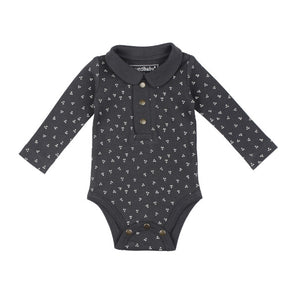 The Lovedbaby Organic Polo Bodysuit, Charcoal Dots features a long-sleeved, organic cotton design in dark gray with small white flower patterns. It has a collared neckline, three front buttons, and ethically made snap closures at the bottom for easy changes.