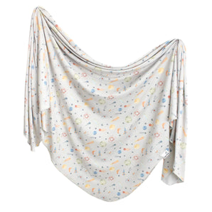 The Copper Pearl Knit Swaddle Blanket in Cosmos is light gray with a colorful nature-themed pattern of leaves, flowers, and berries.