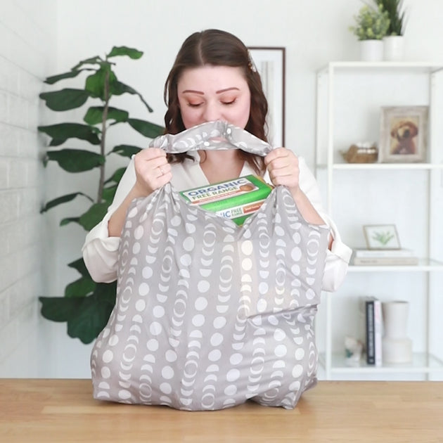 A woman lifting a filled Bumkins Packable Tote Bag full of groceries to show that it can hold up to 50 lbs of items.