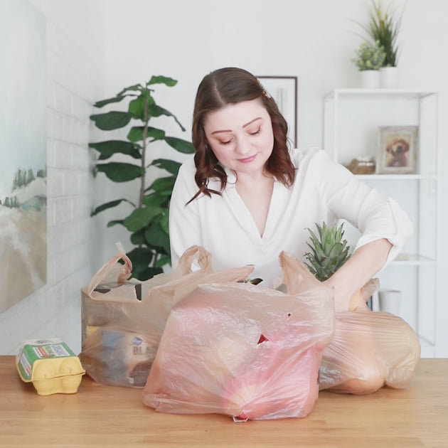 A woman showing how three disposable plastic bags worth of items fit into Bumkins Waterproof Packable Tote Bag.