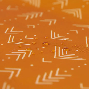 Close-up of water droplets on Bumkins Reusable Snack Bag in bright orange with a white arrow geometric pattern.