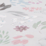 Close-up of Bumkins Starter Bib in a floral, waterproof design with droplets on pink, green, and brown patterns over light gray.