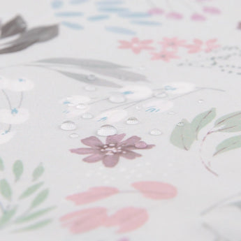 Close-up of Bumkins Starter Bib in a floral, waterproof design with droplets on pink, green, and brown patterns over light gray.