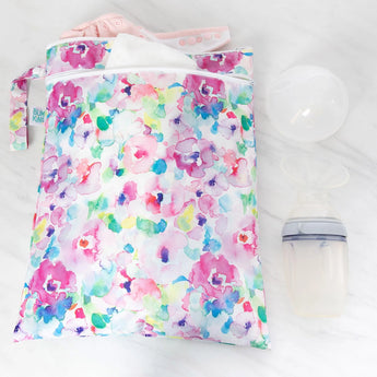 A Bumkins Watercolor Wet/Dry Bag filled with baby items, placed next to a breast pump on a white surface.