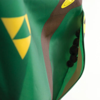 Close-up of Bumkins Sleeved Bib: Zelda™, showcasing waterproof fabric with a geometric pattern in green, brown, yellow, and buttons.