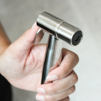 Hand holding the Bumkins Cloth Diaper Sprayer, a sleek stainless steel handheld bidet with adjustable spray pressure.