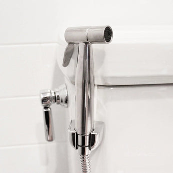 The Bumkins Cloth Diaper Sprayer, a silver wall-mounted bidet with adjustable spray pressure, is ideal for use by a white toilet.