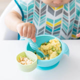 A baby uses the Bumkins Silicone First Feeding Set: Blue to eat scrambled eggs, avocado, and cereal puffs.