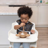 A toddler in a high chair, wearing a bib, enjoys the Bumkins Silicone First Feeding Set: Minnie Mouse Gold.