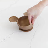 A hand holds a Bumkins Minnie Mouse Gold Feeding Set on a white marble surface.