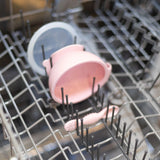 Pink bowl with clear lid and small pink item in dishwasher rack, part of Bumkins Silicone First Feeding Set: Pink.