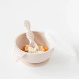 The Bumkins Silicone First Feeding Set in Sand, with lid and spoon, is perfect for mashed food on a white surface.