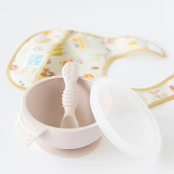 The Bumkins Silicone First Feeding Set in Sand, with lid and spoon, is perfect for self-feeding, paired with a patterned baby bib.