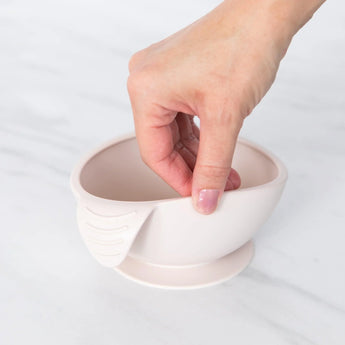 Hand holds Bumkins Silicone First Feeding Set: Sand, featuring a spout and textured grip, on a marble surface.