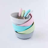 Bumkins Silicone Grip Bowl in gray with pastel food-safe platinum silicone bowls and spoons on a white background.