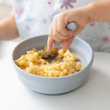 A child enjoys mac and cheese from a Bumkins Silicone Grip Bowl: Gray using a spoon.