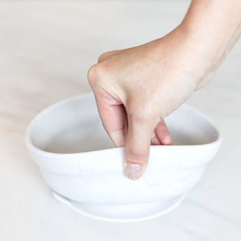 A hand squeezes the soft, flexible Bumkins Silicone Grip Bowl in Marble, ideal for self-feeding toddlers.