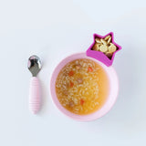 A Bumkins Silicone Grip Bowl cradles soup with rice, veggies, star crackers; a pink-handled spoon rests nearby.