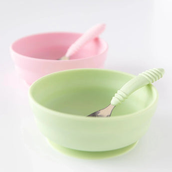 On a white surface: two Bumkins silicone grip bowls with suction bases and spoons; colors: sage and pink.