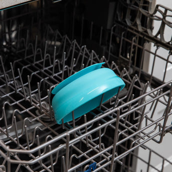 A Bumkins Silicone Grip Bowl: Blue sits in the open dishwasher next to a blue dish rack holding clean dishes.