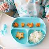 A baby in a dino outfit enjoys rice, sweet potato, and a star treat on Bumkins Silicone Grip Dish: Blue with suction base.