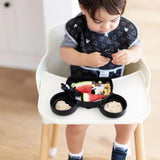 Toddler in highchair, bib on, playing with a black spoon and enjoying oatmeal, fruit, and cereal from Bumkins Mickey Mouse Grip Dish.