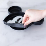 A hand lifts a Bumkins Silicone Grip Dish: Mickey Mouse, ideal for toddler feeding, on a marble countertop.