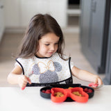 Young girl with long hair sits at a table using a Bumkins Silicone Grip Dish: Minnie Mouse, enjoying food with her fork.