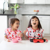 Two kids in Minnie Mouse bibs enjoy their meal with Bumkins Silicone Grip Dish: Minnie Mouse to keep food secure at the table.