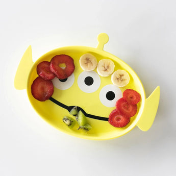 The Bumkins Silicone Grip Dish Toy Story Alien, in yellow, features apple ears, banana eyes, a kiwi mouth, and a strawberry nose. Perfect for toddlers!.