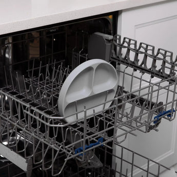 The Bumkins Silicone Grip Dish: Gray sits on the top rack of an open dishwasher.