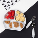 The Bumkins Silicone Grip Dish: Gray holds watermelon, banana slices, and waffle pieces with a spoon and fork on a black/white background.