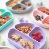 Bumkins Silicone Grip Dish in Lavender holds snacks like pasta, toast, and fruit; made from food-safe silicone for kids meals.