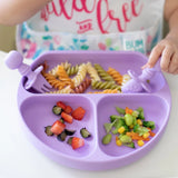 A child enjoys colorful food from Bumkins Silicone Grip Dish: Lavender while wearing a bright shirt.