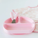 Pink Silicone Grip Dish and matching utensils from Bumkins with a floral bib, perfect for toddler self-feeding.