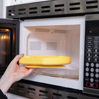 A person placing a yellow Bumkins Silicone Grip Dish: Pineapple into an open microwave.