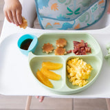 A child enjoys breakfast with their Silicone Grip Dish: Sage by Bumkins, having scrambled eggs, orange slices, bacon, pancakes & syrup.