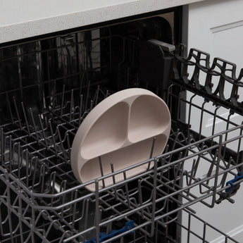 A Bumkins Silicone Grip Dish: Sand is ready for a thorough clean on the top rack of an open dishwasher.