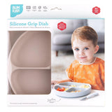 A child with an orange bib sits by a Bumkins Silicone Grip Dish in Sand, featuring food-safe platinum silicone and a sturdy suction base.