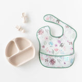 Bumkins Silicone Grip Dish: Sand with suction base, floral baby bib, and 2 utensils on a white background.