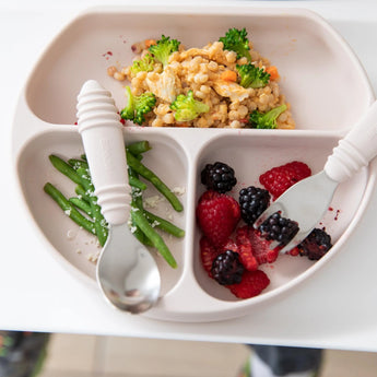 The Bumkins Silicone Grip Dish: Sand with a suction base holds couscous, broccoli, green beans, berries alongside a spoon and fork.