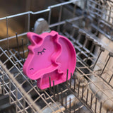 The pink Silicone Grip Dish Special Edition: Unicorn by Bumkins adds whimsy to your dishwasher, nestled among the racks.