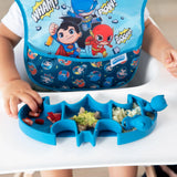 A child enjoys snacks from a Bumkins Silicone Grip Dish: Batman Blue, wearing a superhero-themed bib at the high chair.