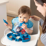 A baby in a superhero bib enjoys meals from Bumkins Batman Blue Silicone Grip Dish while an adult watches over.