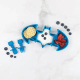 Bumkins Silicone Grip Dish: Batman Blue bat-shaped plate with waffles, yogurt, berries, fork & spoon on white marble.