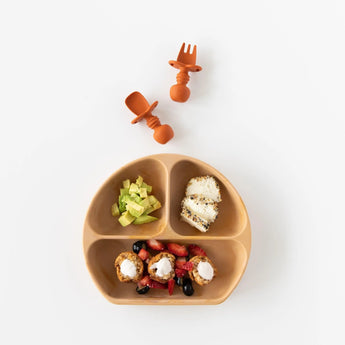 Bumkins Silicone Grip Dish: Wood Grain holds avocado, toast, and yogurt. Includes a baby fork and spoon, all on a food-safe surface.