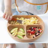 A child enjoys scrambled eggs, avocado, and fruit from a Bumkins Silicone Grip Dish: Wood Grain with a secure suction base.